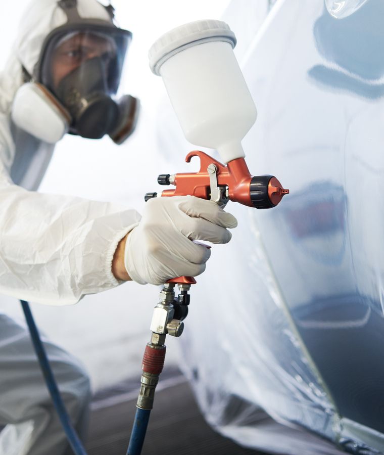 Ein Lackierer lackiert ein Fahrzeug mit einer Sprühpistole